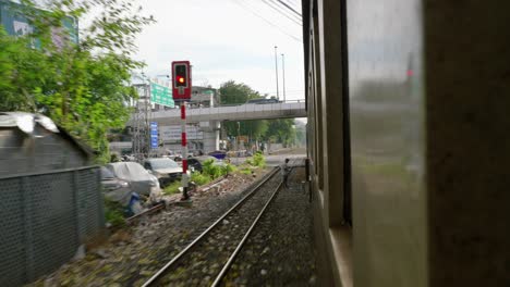 Passenger-view-looking-out-window-of-moving-train-traveling-through-city,-Thailand