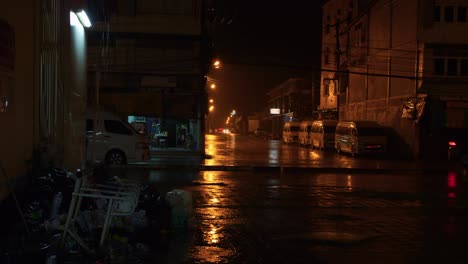 Street-lights-dimly-illuminate-road-on-a-wet-and-rainy-night-as-car-passes-by,-Thailand