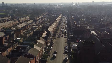 Aerial-view-reveals-rows-of-historic-terraced-houses-in-Dentons-Green,-St-Helens-with-a-long-road-leading-towards-the-bustling-town-skyline