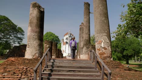 Woman-tourist-walking-up-stone-steps-to-ruins-of-religious-statue-between-ancient-pillars,-Thailand