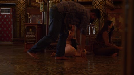 Asian-couple-sitting-on-floor-in-Buddhist-temple-praying-to-Buddha-with-other-people,-Thailand