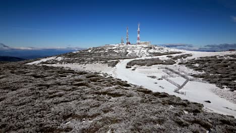 Aerial-shot-ascending-a-snowy-mountain-towards-some-antennas-at-the-top-of-the-mountain-in-Manzaneda,-Galicia