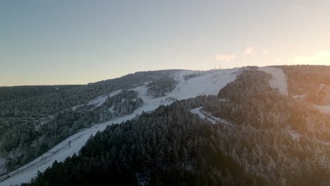 Aerial-backward-cinematic-shot-flying-over-a-snowy-mountain-with-many-trees-in-Manzaneda,-Galicia