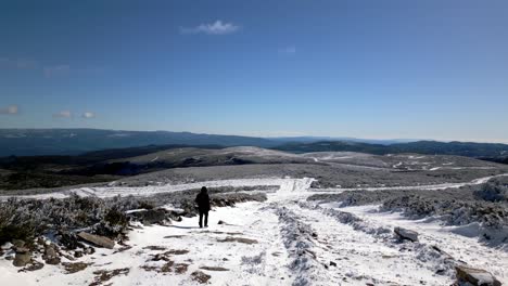 Ascending-aerial-shot-flying-over-a-snowy-path-on-which-a-person-walks-in-a-mountainous-landscape-in-Manzaneda,-Galicia