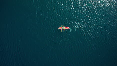 Two-people-paddle-orange-kayak-in-wavy-water,-wide-overhead-aerial