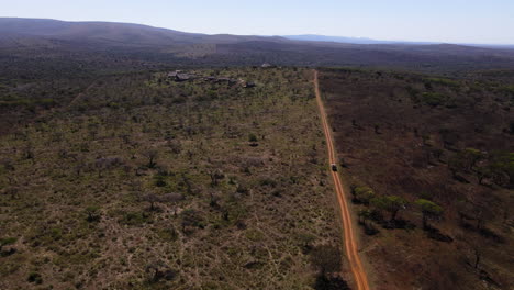 Ariel-drone-shot-of-a-safari-vehicle-driving-down-a-dirt-road-showing-one-fire-burnt-area-and-an-unburnt-area-in-the-winter-months-of-Africa-searching-for-wild-animals