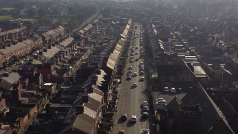 Aerial-descending-view-reveals-rows-of-historic-terraced-houses-in-Dentons-Green,-St-Helens-with-a-long-road-leading-towards-the-bustling-town-at-sunrise