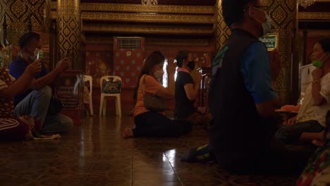 Men-and-women-praying-to-Buddha-inside-Buddhist-temple,-Wat-Phra-Sri-Rattana-Mahathat,-Thailand
