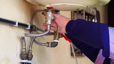 Person-handling-some-pipes-of-an-electric-water-heater-with-a-wrench