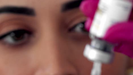 Close-up-of-a-Latina-doctor's-face-as-she-fills-a-syringe-from-a-vial---close-up-rack-focus
