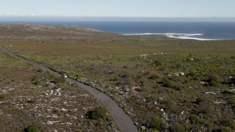 Vista-Aérea-De-Sudáfrica-Cabo-De-Buena-Esperanza-Coche-Conduciendo-Por-Una-Carretera-Hacia-El-Mar
