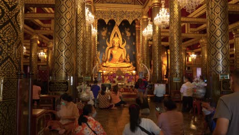 Titling-view-from-behind-people-praying-to-praying-to-Buddha-statue-in-Buddhist-temple,-Thailand