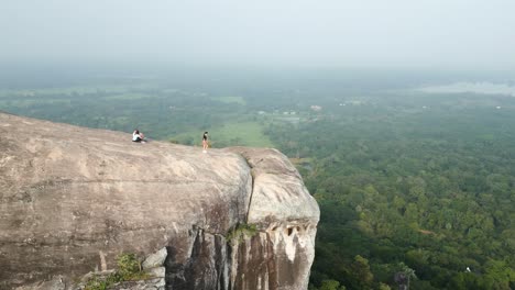 Aerial-drone-shot,-Pidurangala-Mountain-Rock-with-a-woman-walking-on-the-edge