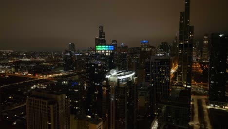 Aerial-view-in-front-of-the-illuminated-The-Paragon-building,-cloudy-night-in-Chicago,-USA---Ascending,-drone-shot