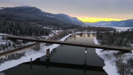 Drone-Flyover-of-Snowy-Thompson-River-and-Highway-1-with-Sunset-Sky-in-the-Background