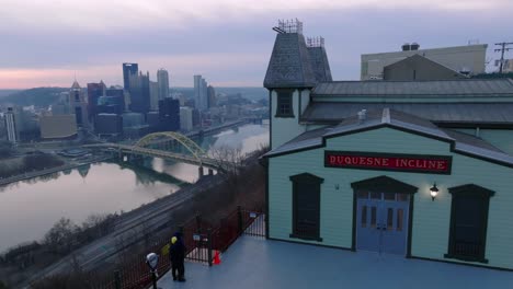 Couple-watching-sunrise-over-Pittsburgh-skyline-from-Duquesne-Incline-building-atop-Mt-Washington-in-Pittsburgh,-Pennsylvania