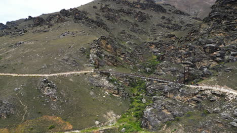 Aerial,-outdoor-biking-bridge-trail-connecting-mountain-valley,-rocky-cliffs