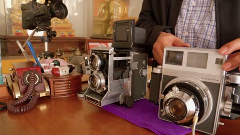 Man-operating-classic-old-cameras,-Mamiya-C220-Professional-and-Press-Super-23-on-table