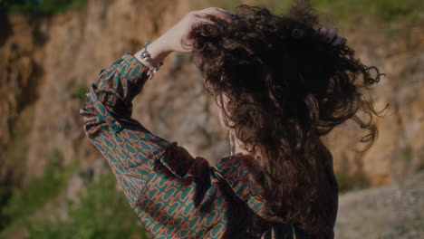 A-woman-in-a-shirt-ruffles-her-curly-hair-and-observes-an-old-quarry