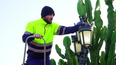 electrician-in-work-clothes-fixing-a-lamppost-outside-a-villa-with-a-cactus-nearby