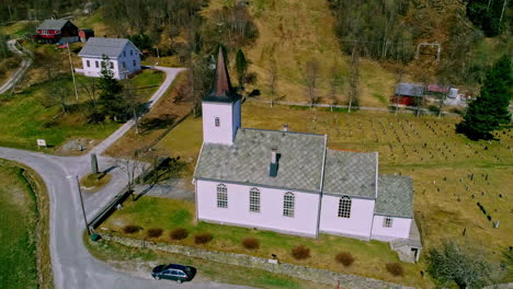 Old-church-building-with-cemetery-in-Norway,-aerial-orbit-view