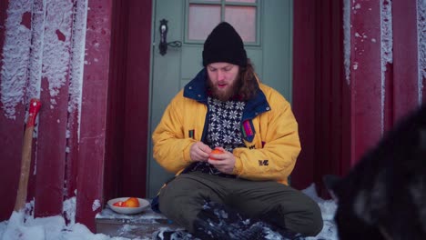 Person-Peeling-And-Eat-Orange-Fruit-Outside-With-His-Dog-During-Winter
