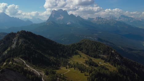Aerial-shot-over-a-green-and-wooded-hilly-landscape-with-a-blue-and-cloudy-horizon-in-Monte-rite,-Dolomites,-Italy