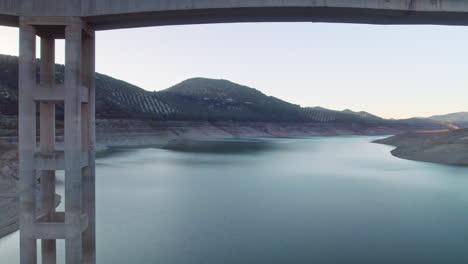 Drone-flying-backwards-and-under-the-bridge-on-the-reservoir-of-Iznájar,-Córdoba,-Spain