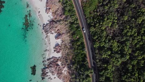 Topdown-aerial-of-car-driving-next-to-the-crystal-clear-waters-of-Eagle-Bay