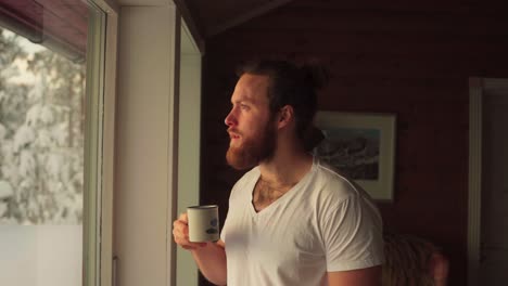 Bearded-Caucasian-Guy-Is-Drinking-Coffee-Inside-The-Winter-Cottage
