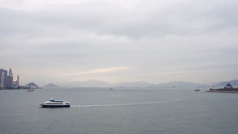 Ferry-travels-by-Victoria-Harbour-in-cloudy-Hong-Kong,-hilly-horizon