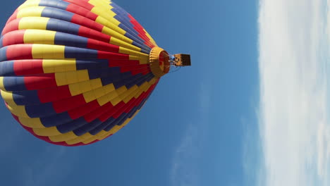 Vertical-Aerial-View-of-Colorful-Hot-Air-Balloon-Flying-Under-Blue-Sky-on-Sunny-Day,-Drone-Shot