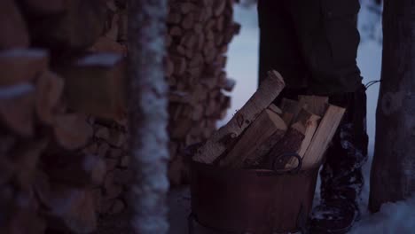 Man-Standing-Next-To-Chopped-Firewood-In-Rusty-Bucket-In-Winter
