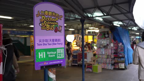 Cartel-En-La-Estación-De-Autobuses-Turísticos-En-Hong-Kong-Y-Gente-Caminando-Detrás