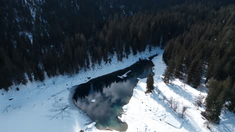 Aerial-View-Of-Calm-Caumasee-Lake-Surrounded-By-White-Snow-And-Conifer-Trees