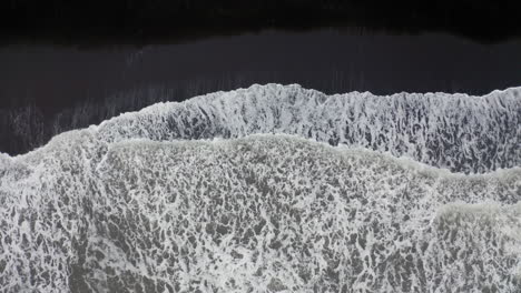 Luftaufnahme:-Von-Oben-Nach-Unten-Ansteigende-Aufnahme-Von-Wellen,-Die-Sich-Am-Schwarzen-Sandstrand-In-Island-Brechen