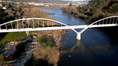 Toma-Aérea-Sobre-Un-Puente-En-El-Río-Miño-En-España,-Gran-Vegetación,-Horizonte-Con-Montañas-Y-Cielo-Azul