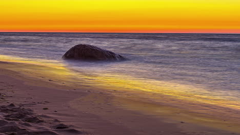 Orangefarbener-Sonnenuntergangshimmel-über-Der-Sandigen-Meeresküste-In-Einsamen-Felsbrocken,-Fusionszeitraffer