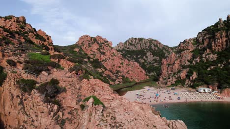 Aerial-reveal-of-tourist-on-a-remote-beach-in-a-rocky-bay-Sardinia-coast