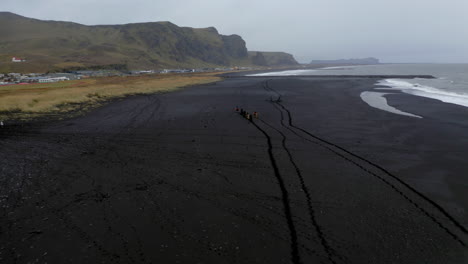 Aerial:-Flying-towards-group-of-tourists-riding-horses-on-the-black-sand-beach-of-Vik-in-Iceland