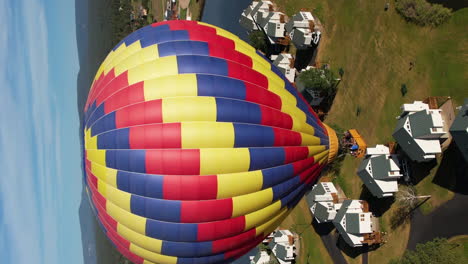 Vertical-Aerial-View-of-Colorful-Hot-Air-Balloon-Flying-Above-Landscape,-Drone-Shot