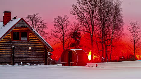Fiery-red-sunset-over-a-cabin-and-sauna-on-a-foggy,-misty-winter-evening---surreal-time-lapse