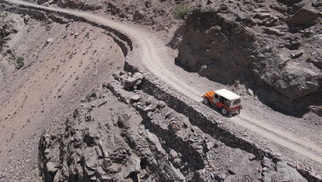 Aerial-View-of-Off-road-Vehicle-Moving-on-Dangerous-Mountain-Pass,-Dirt-Road-in-Northern-Pakistan,-Drone-Shot