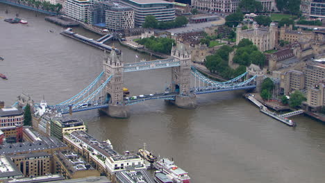 Rotierende-Luftaufnahme-Der-Tower-Bridge-Mit-Autos,-Die-Zusammen-Mit-Einem-Kriegsschiff-In-Der-Themse-Fahren