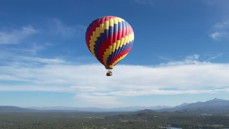 Aerial-View-of-Multicolored-Hot-Air-Balloon-Parachute-Flying-Above-Landscape-and-Lake-on-Sunny-Day