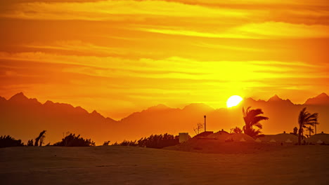 Zeitraffer-Einer-Sandigen-Wüstenlandschaft-Mit-Palmen-Unter-Einem-Orangefarbenen-Und-Roten-Himmel-Mit-Wolken-Bei-Sonnenuntergang