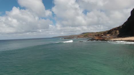 FPV-drone-shot-moving-backwards-around-a-small-rocky-island-and-over-a-beach-in-sunny-Hawaii