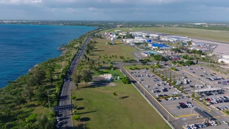 Aerial-flight-over-highway-with-traffic-and-parking-area-of-Las-Américas-International-Airport-during-sunny-day-on-Dominican-Republic