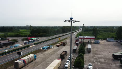 Drone-aerial-footage-over-a-highway-with-traffic-passing-by-and-track-parking-area,-captured-in-Hebei-Province,-China