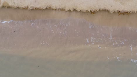 Sanfte-Wellen-Am-Strand-Mit-Klarem-Wasser,-Das-Gegen-Eine-Erodierte-Landschaft-Prallt